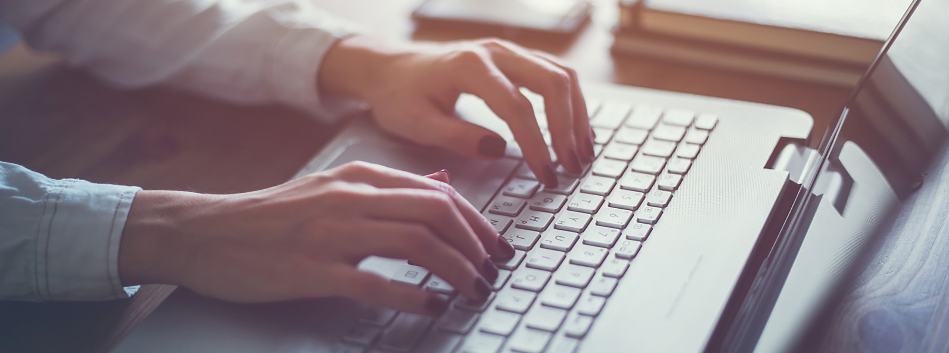 A person s hands are visible, typing on a laptop computer placed on a desk.