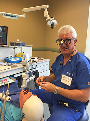 In the image, a man in a blue scrub is sitting at a dental chair with various tools and equipment around him. He appears to be engaged in some form of medical or dental examination or procedure.