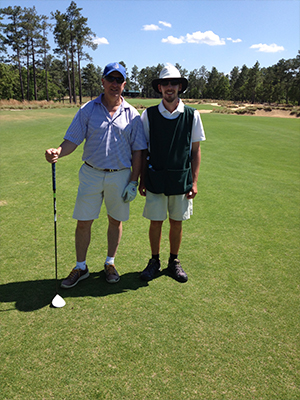 A man and a woman standing on a golf course, with the man holding a golf club and both of them posing for a photo.