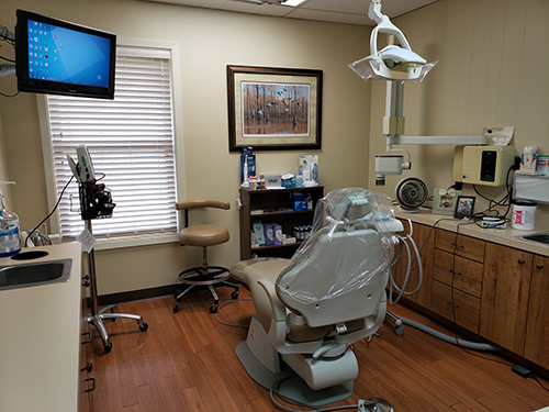 A dental office interior with a dentist chair, equipment, and a large screen displaying a presentation.