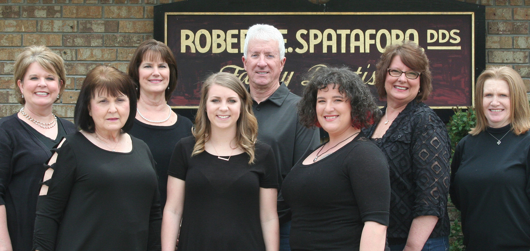 The image shows a group of people, likely a choir or singing ensemble, posing for a photograph in front of a sign that reads  Robert Spataro DDS.