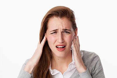 A young woman with blonde hair, wearing a white shirt and dark pants, is holding her hand to her ear, possibly in disbelief or astonishment.