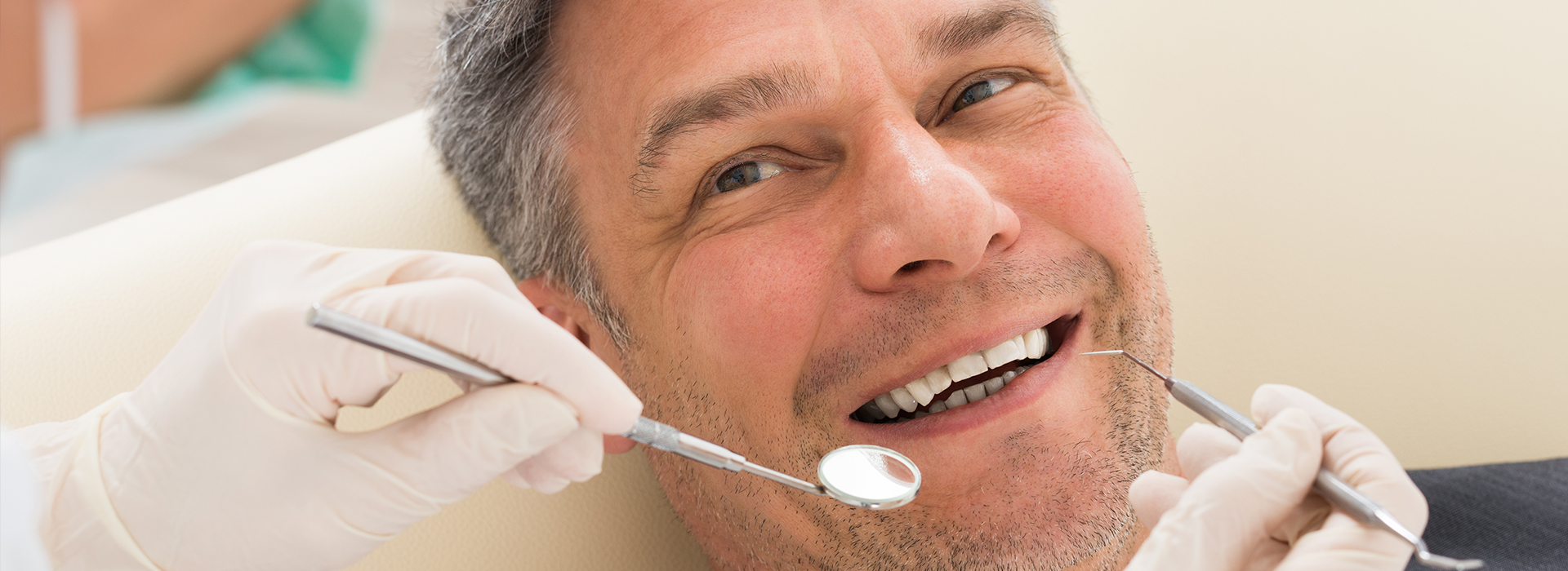 A man seated in a dental chair with a smile, receiving dental care from a professional.