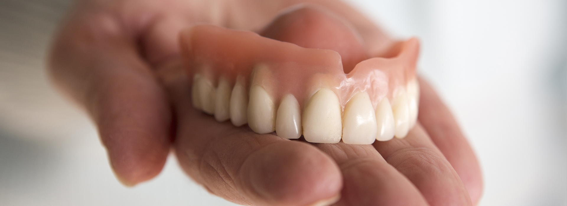 An adult hand holding a set of dentures, showcasing the upper and lower false teeth.