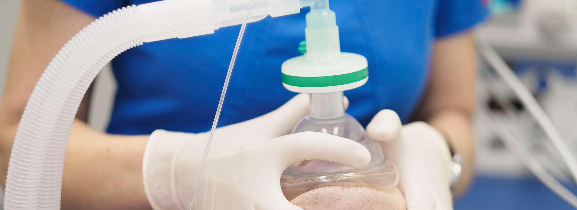 The image depicts a person in a white lab coat holding a clear plastic syringe containing a greenish-brown liquid, presumably a medication or solution, with the syringe attached to a transparent tube and connected to a machine.