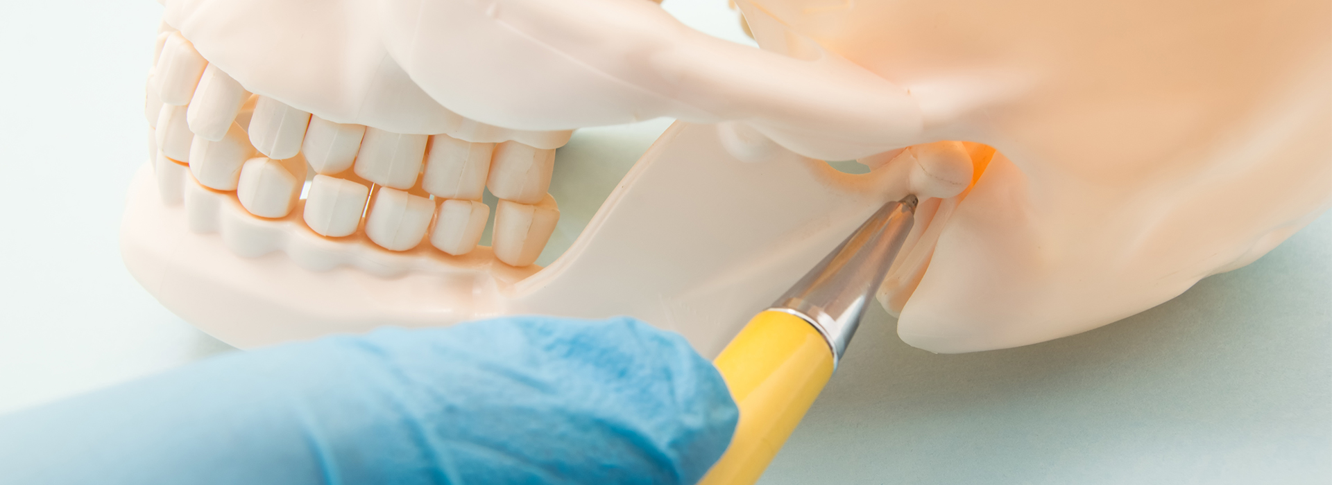 An image of a dental procedure being performed, featuring a model human head with teeth and a yellow instrument in the process of fixing a tooth.