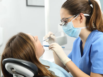 The image shows a dental hygienist performing a cleaning procedure on a patient in a dental office.