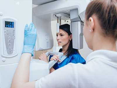 A woman in a blue jacket stands next to a large, modern medical imaging machine, with another person looking at the equipment.