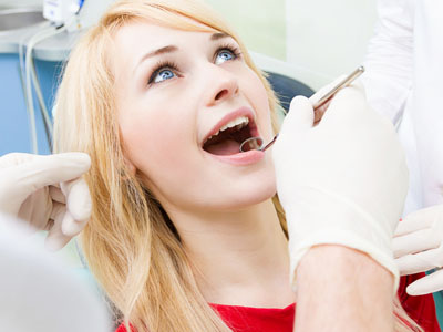 A woman in a dental chair receiving dental care, with a dental hygienist performing the procedure.