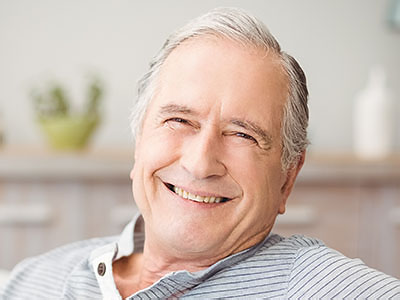 The image shows an older man with a smile, sitting comfortably in a chair.