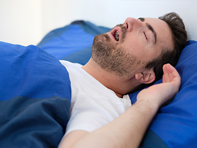 The image depicts a man lying in bed with his eyes closed, suggesting he is asleep or resting.