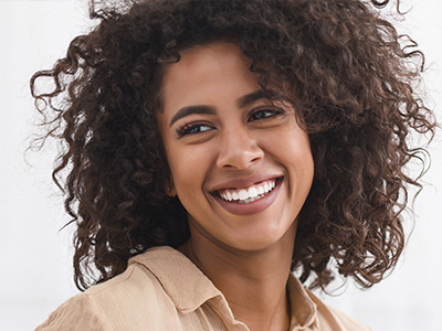 The image features a smiling woman with curly hair, wearing a beige top and looking directly at the camera.